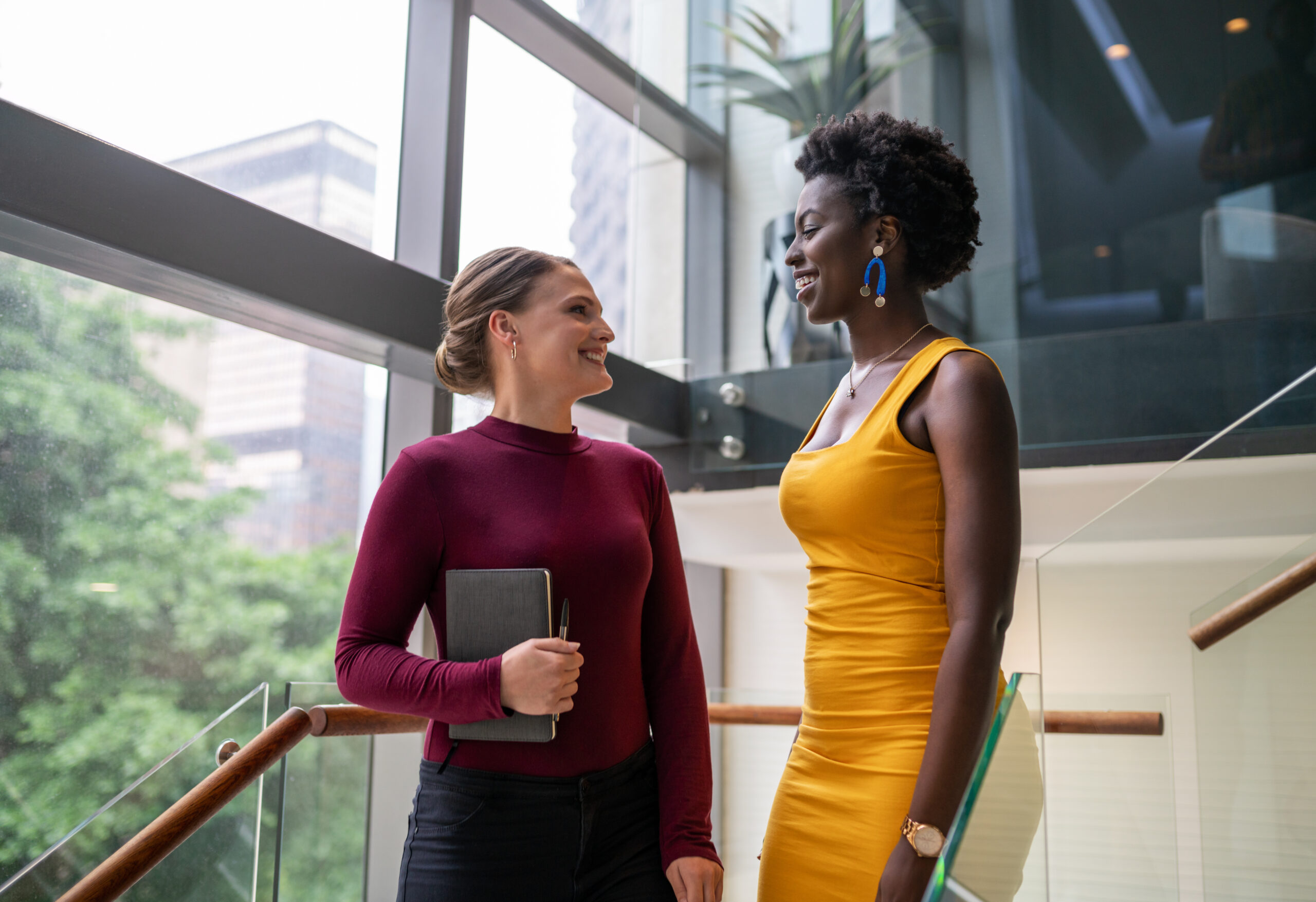 Two diverse young women smiling and talking about PCOS on the stairs of a modern office | Conceive NJ